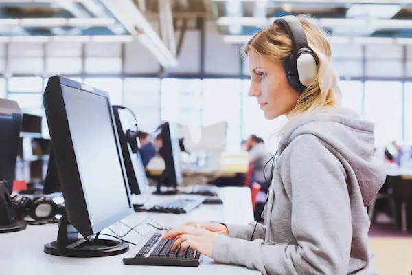 Frau sitzt mit Kopfhörern vor Computer und absolviert einen Sprachtest
