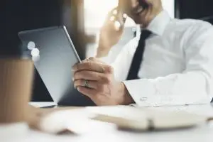 Australischer Investor sitzt am Schreibtisch, telefoniert und liest auf Tablet