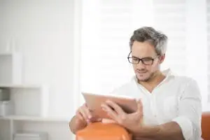 Mann sitzt auf der Couch und liest auf einem Tabletcomputer ein Visumsgutachten