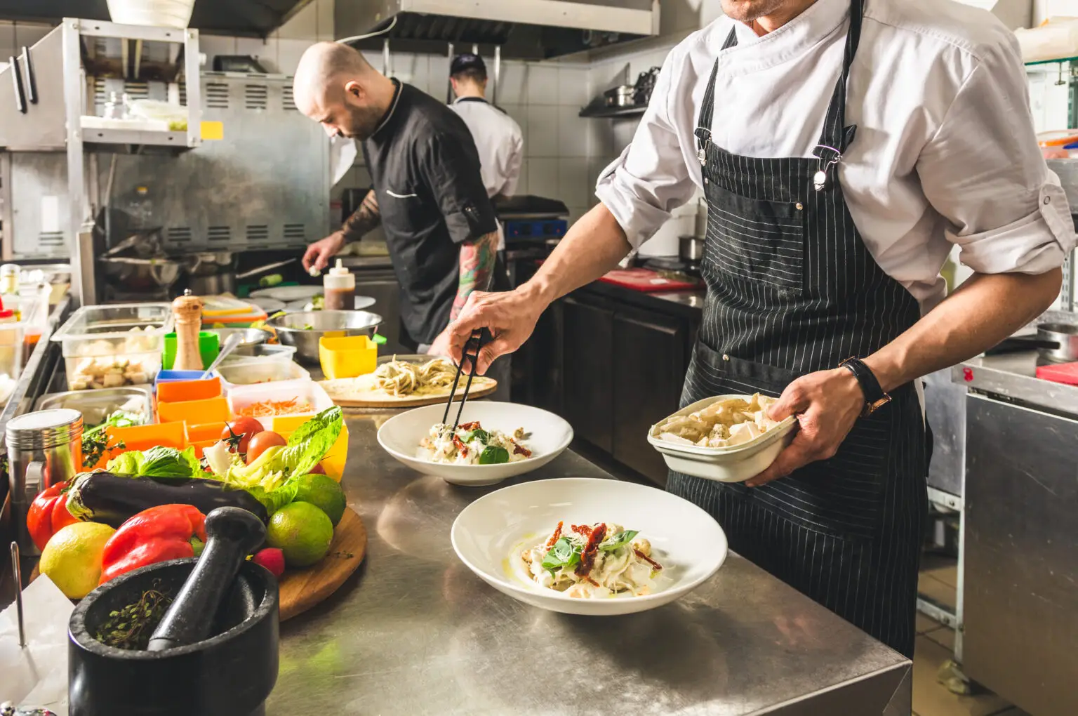 Professional chef cooking in the kitchen restaurant at the hotel, preparing dinner. A cook in an apron makes a salad of vegetables and pizza