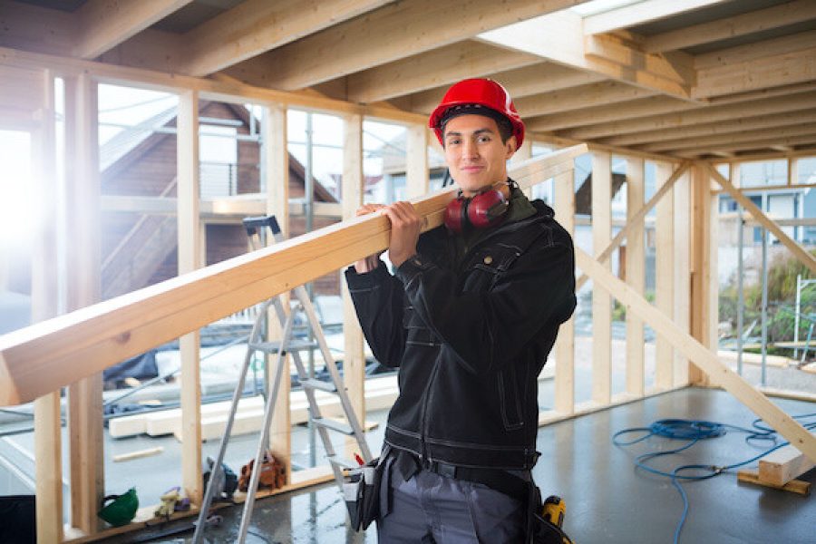 Portrait of male young carpenter carrying wood on shoulder at construction site